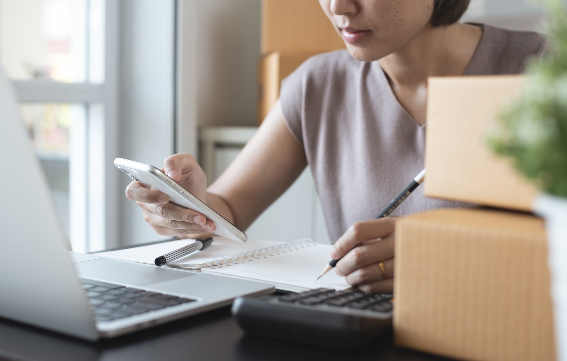 Small business, E-commerce, online market concept. Smiling young asian woman entrepreneur checking customer's order on mobile phone and taking note